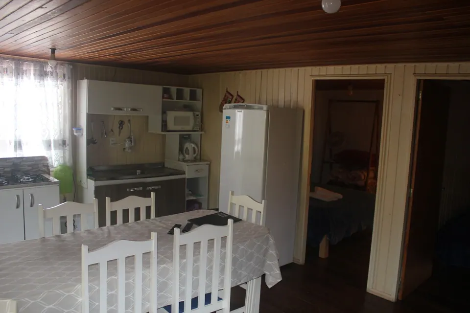 Cozinha e sala de jantar conjugadas, com mesa de toalha xadrez, cadeiras brancas, geladeira e forro de madeira